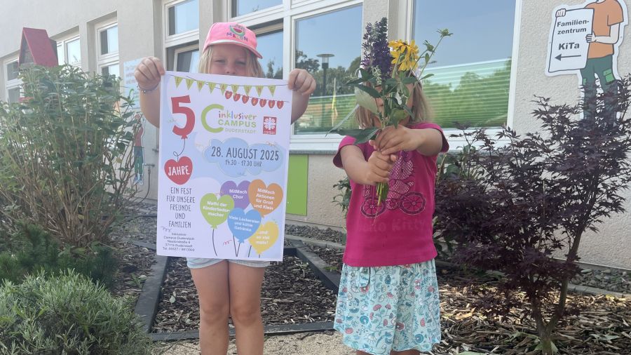 Zwei Kinder aus dem Inklusiven Campus zeigen das Festplakat und halten einen Blumenstrau8 als Willkommensgruß. | Foto: Isabel Lubojanski / Caritas