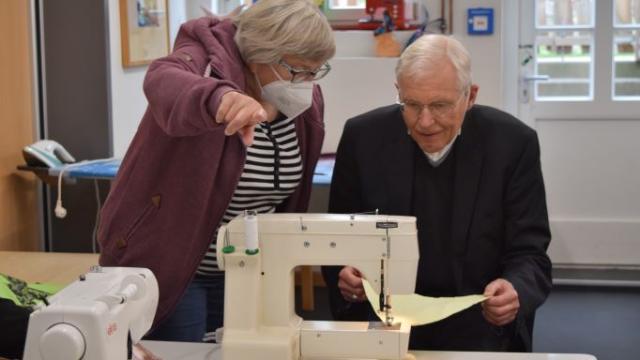 Weihbischof Dr. Nikolaus Schwerdtfeger näht unter Anleitung von Bärbel Schneegans einen Wimpel. Zum Godehardtag am 9. Juli 2022 in Duderstadt soll eine Wimpelkette die Straßen schmücken. | Foto: Johannes Broermann / cps