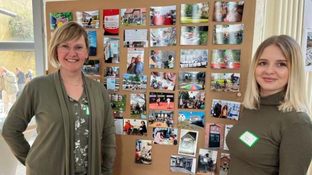 Anna Holland (l.) und Nicole Begunov stehen vor einer Stellwand, auf der einige Eindrücke der bisherigen Gemeinwesenarbeit dargestellt werden. | Foto: Caritas