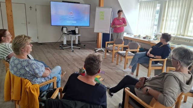Das Foto zeigt einen Stuhlkreis mit Teilnehmenden und die Kursleiterin Leandra Conradi stehend.