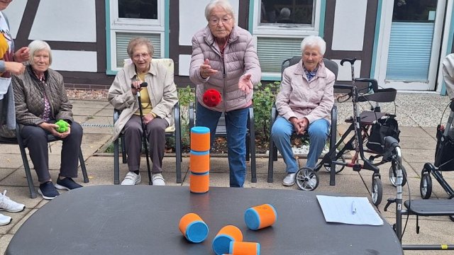Das Bild zeigt eine Frau, die einen roten Ball auf einen Turm aus Schaumstoffquadern wirft.