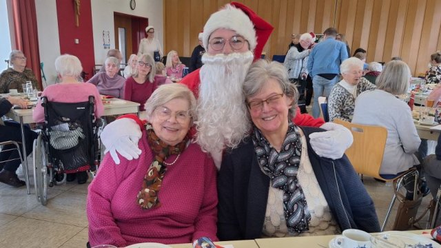 Das Foto zeigt, wie zwei sitzende Frauen vom Nikolaus in den Arm genommen werden.
